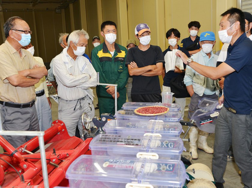 実際に播種機を使って播種量の調整方法を説明するＪＡ福井基幹支店営農指導課の担当職員（写真右）（ＪＡ福井南部米検査場で）
