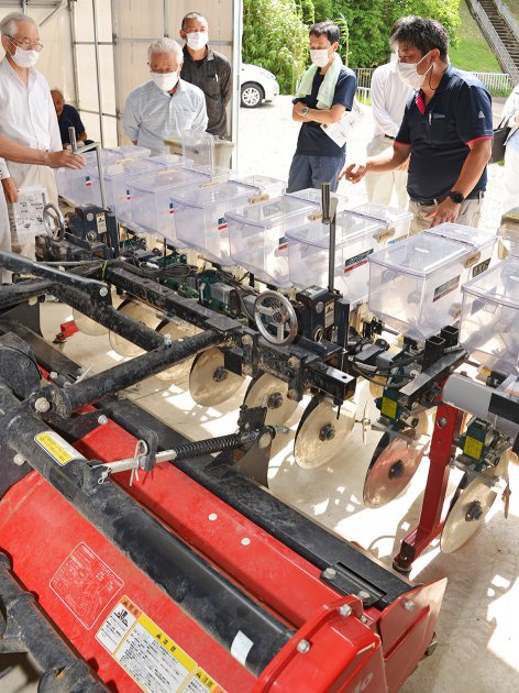 播種機を実際に見ながら小豆の播種量の調整方法を確認する参加者たち（ＪＡ福井西部支店管内の農業機械格納庫で）